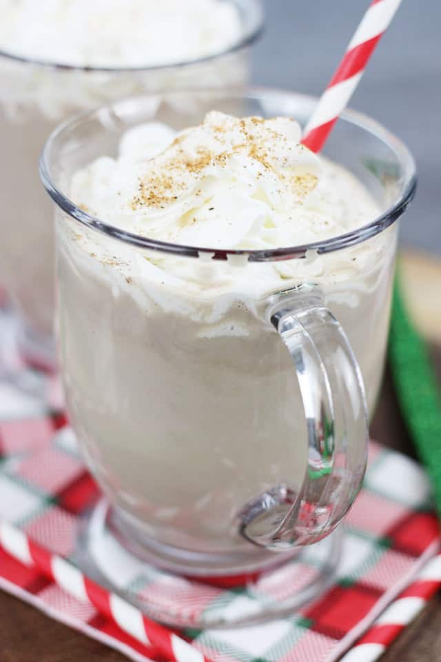 A glass mug filled with chocolate eggnog with a red and white straw