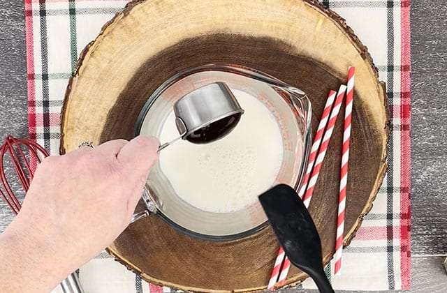 Adding chocolate syrup to milk in a glass measuring cup