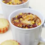Two white soup mugs filled with crockpot chicken chili with cornbread muffins next to them