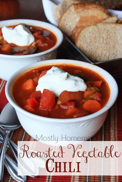 Roasted vegetable chili in two white bowls topped with sour cream