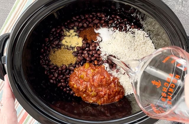 Adding ingredients for crockpot black beans and rice to a black crockpot
