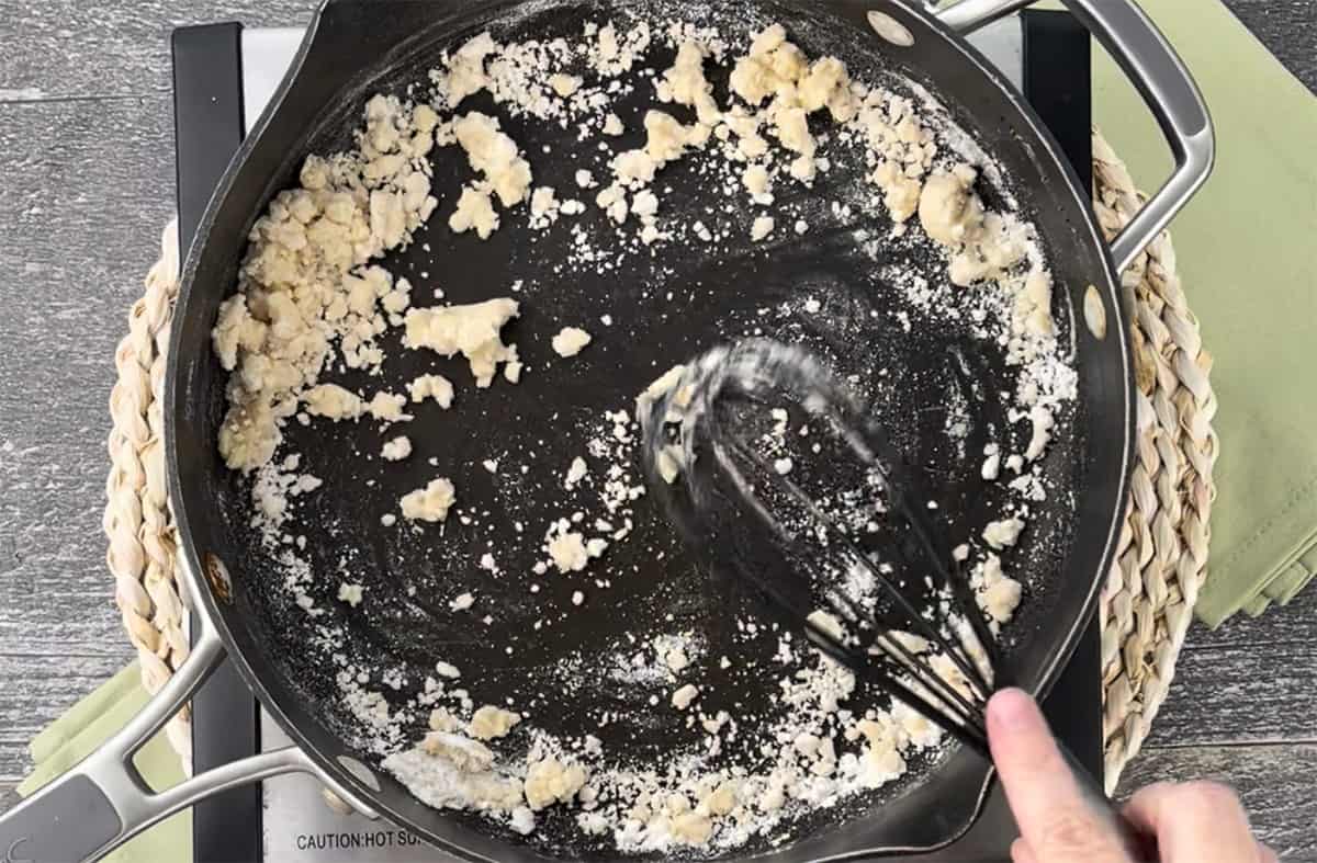 Whisking flour into melted butter in a skillet.