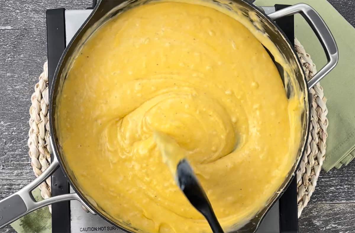 Stirring the cheese sauce with a spatula in a skillet.