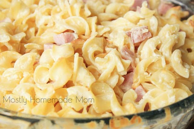 A close up picture of ham and noodle casserole being served in a glass baking dish
