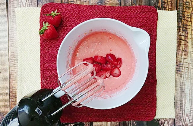 Adding strawberries to the cake batter in a white bowl
