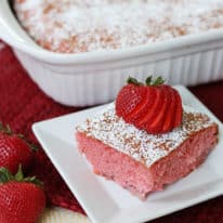 A piece of strawberry jello cake on a white plate with the cake pan in the background