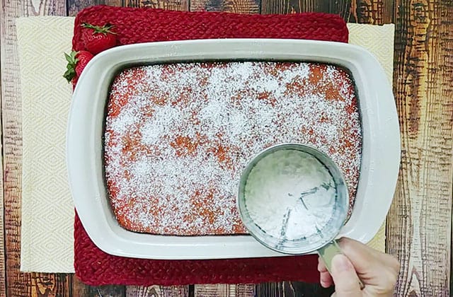 Sprinkling powdered sugar on top of strawberry cake