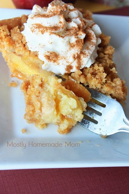 A fork taking a slice of apple custard pie on a white plate