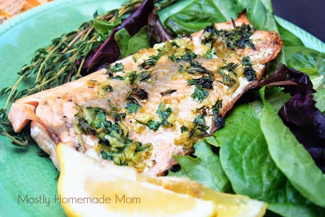 A grilled lemon salmon fillet topped with herbs on a green plate being served