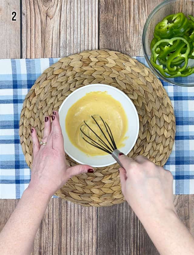 Whisking Dijon mustard and Italian salad dressing in a white bowl with a black whisk