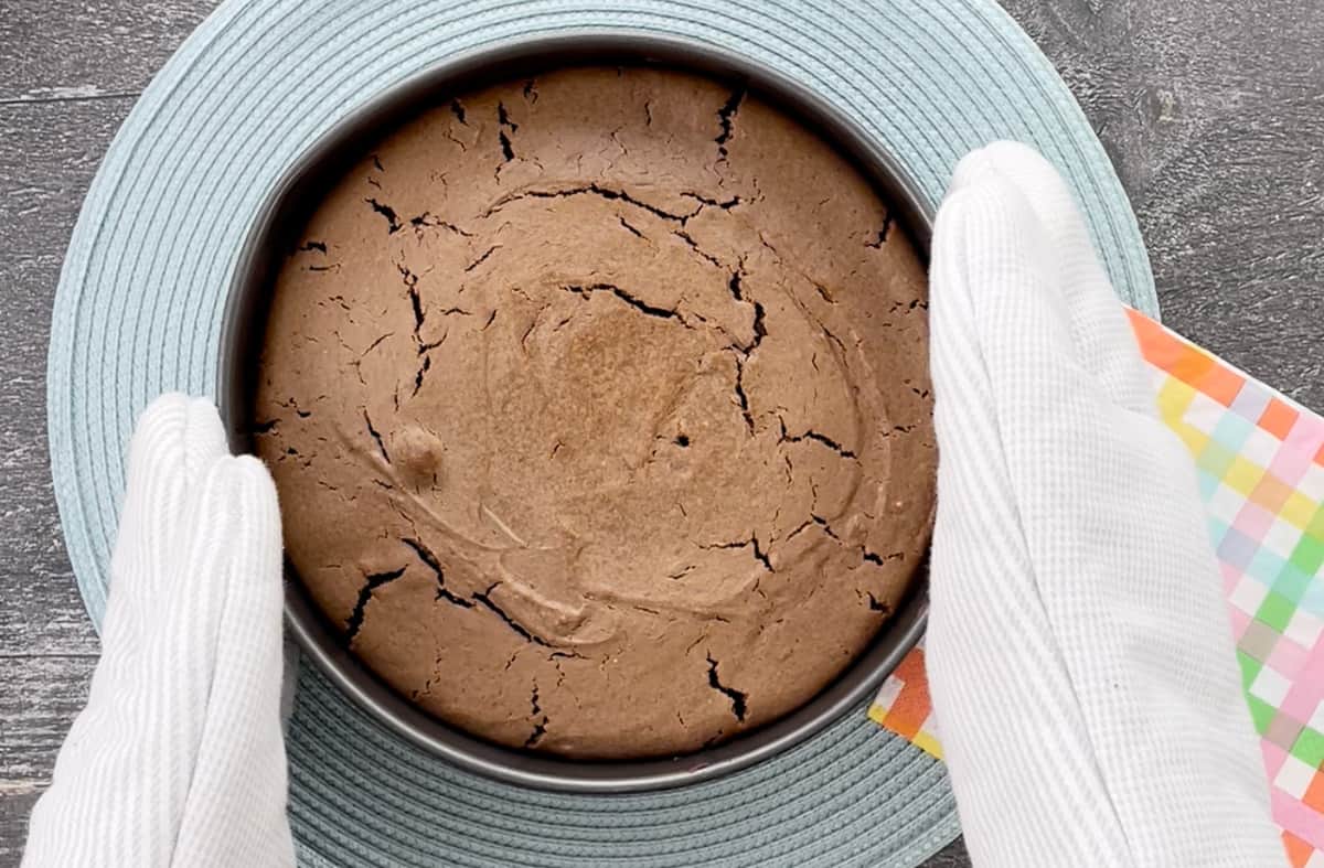 Removing the brownie cheesecake from the oven using oven mitts.