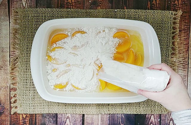 Sliced peaches in a baking dish with cake mix being sprinkled on top