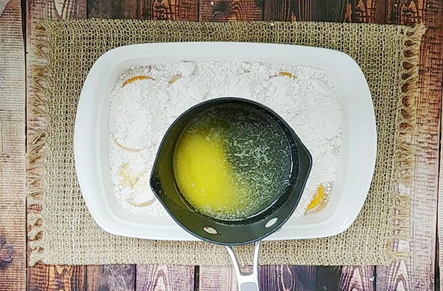 Drizzling melted butter from a saucepan over cake mix in a baking dish