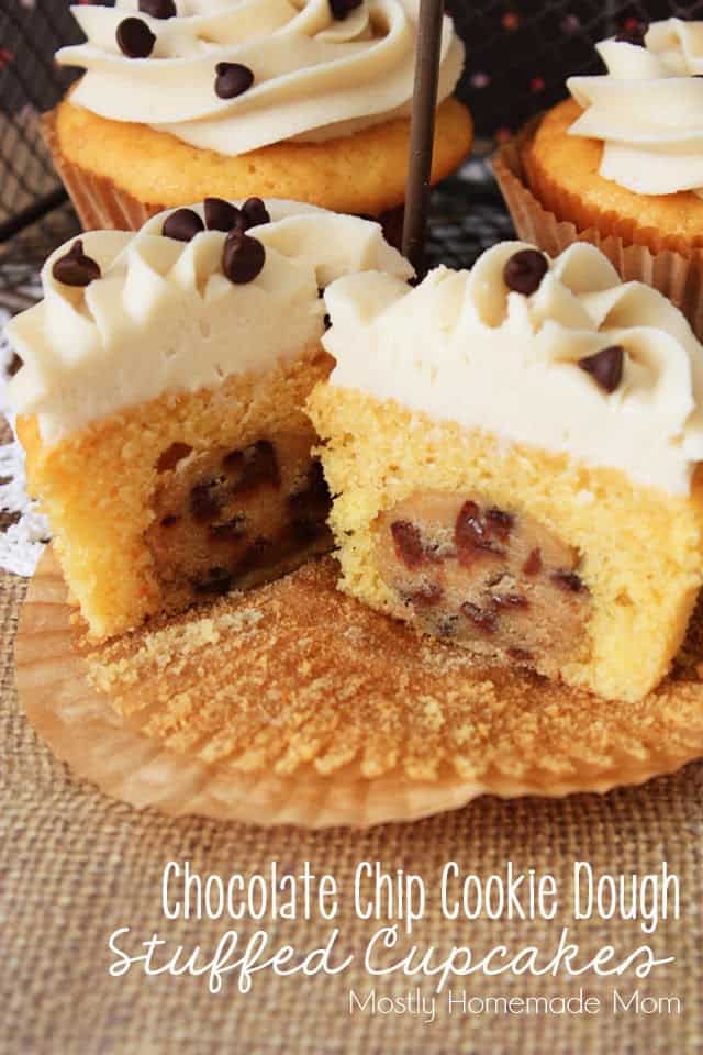 A cookie dough cupcake sitting on a cupcake liner sliced in half to show the cookie dough in the center