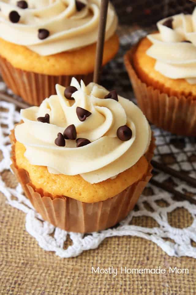 A close up picture of a cookie dough cupcake in a brown paper cupcake liner topped with mini chocolate chips