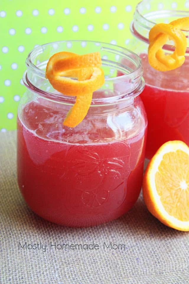 A mason jar glass filled with orange cranberry Bellini with an orange peel garnish