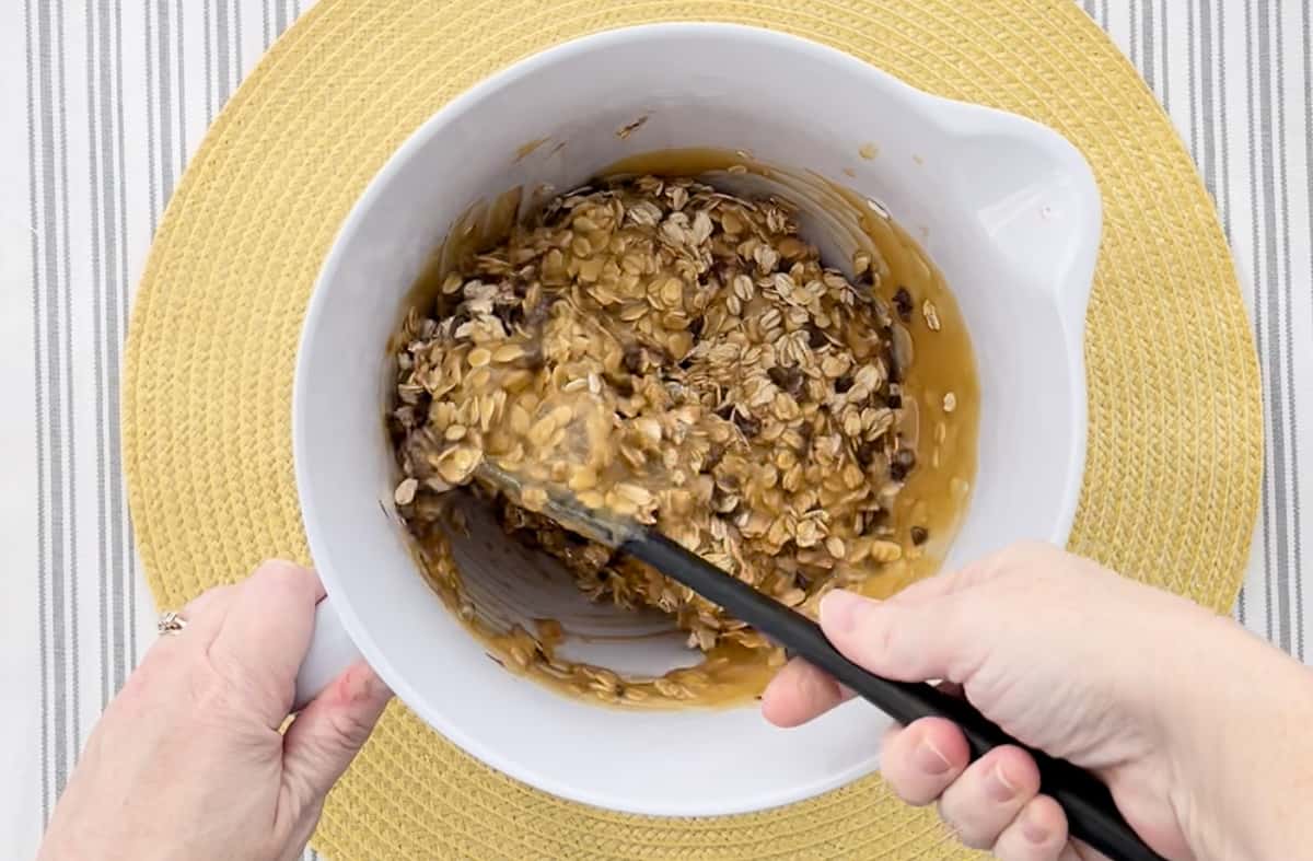 Stirring the granola bar ingredients in a large white mixing bowl.