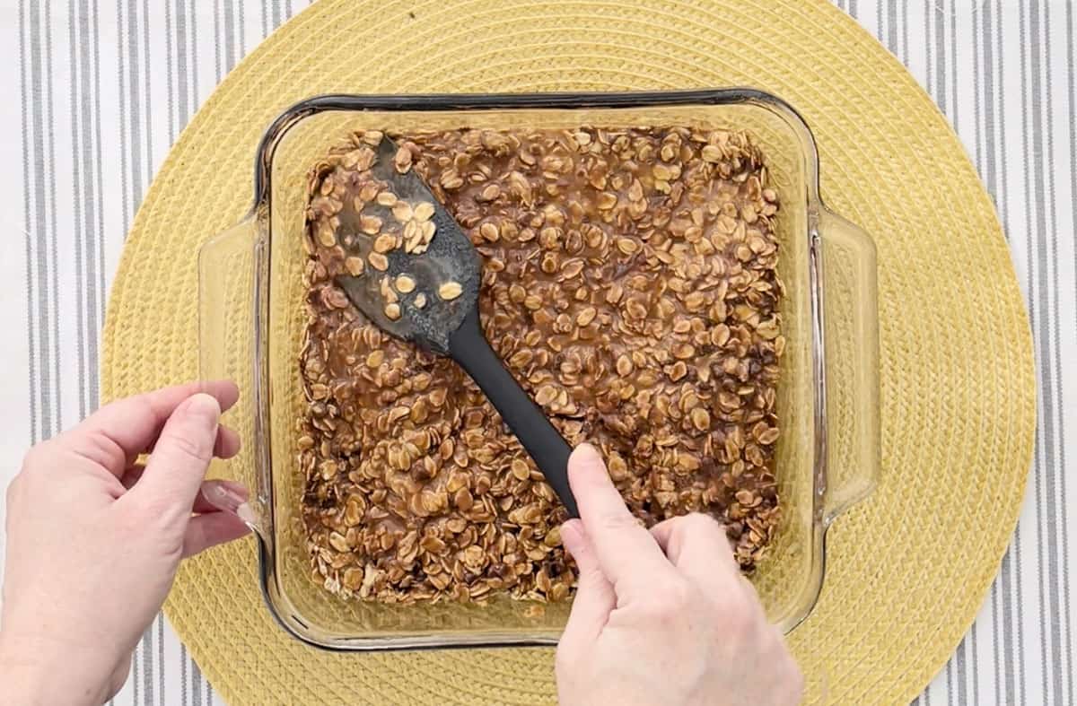 Pressing the granola bar mixture into a glass baking dish with a spatula.