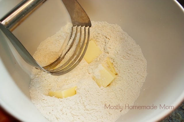 Using a pastry blender in a white mixing bowl to blend cold butter into flour