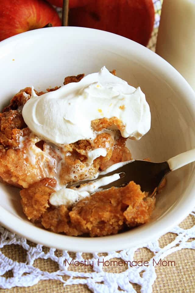 A slice of crock pot apple pie with a fork mixing it with whipped cream