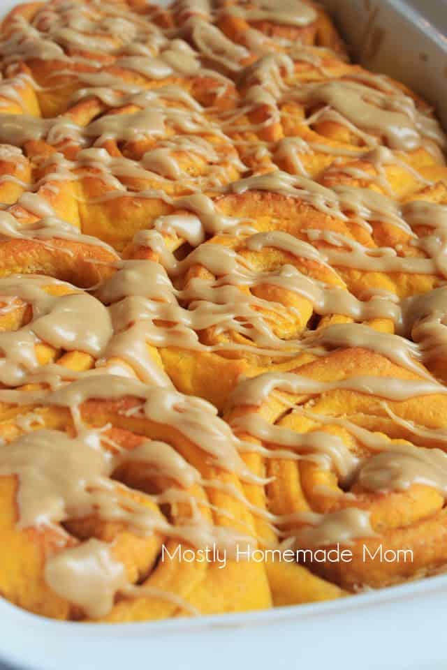 A baking dish of pumpkin cinnamon rolls with salted caramel frosting drizzled on top