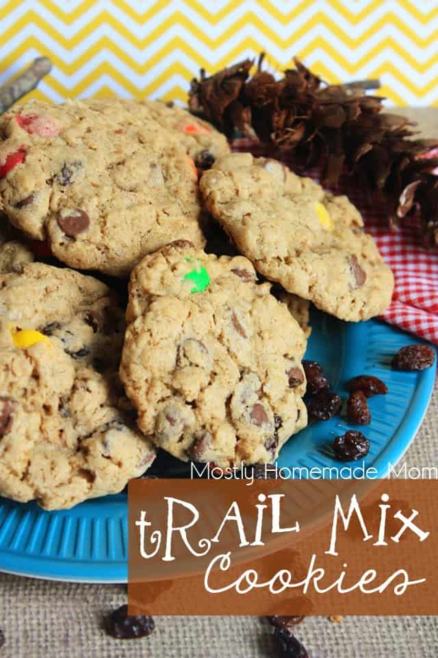 A blue plate filled with trail mix cookies with a pine cone in the background