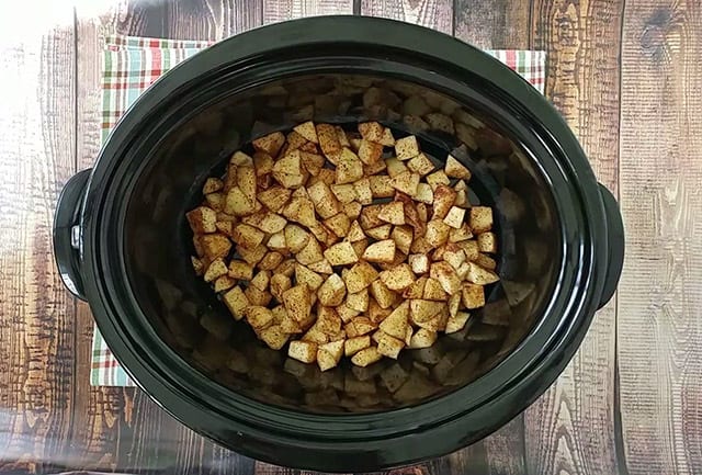 Chopped apples in the bottom of a crock pot with spices