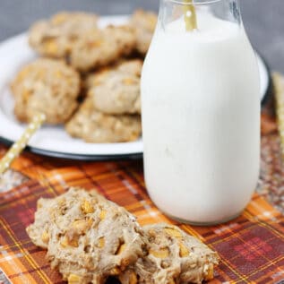 Oatmeal butterscotch cookies on a plaid napkin with a glass of milk.