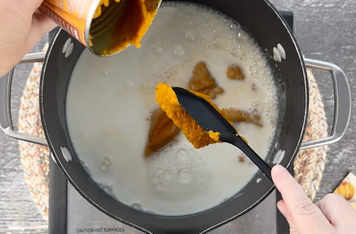 Adding pumpkin puree to a pot on the stove.