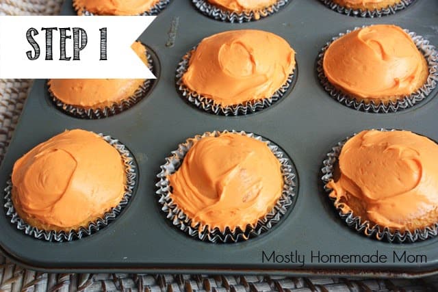 Cupcakes with orange frosting sitting in a metal muffin tin