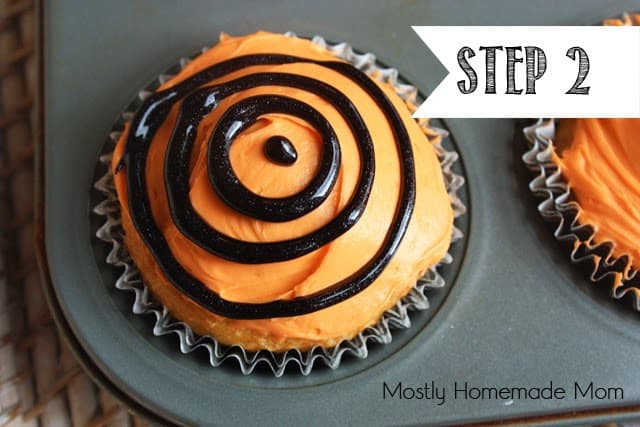 A cupcake in a muffin tin with orange frosting and black circle frosting on top