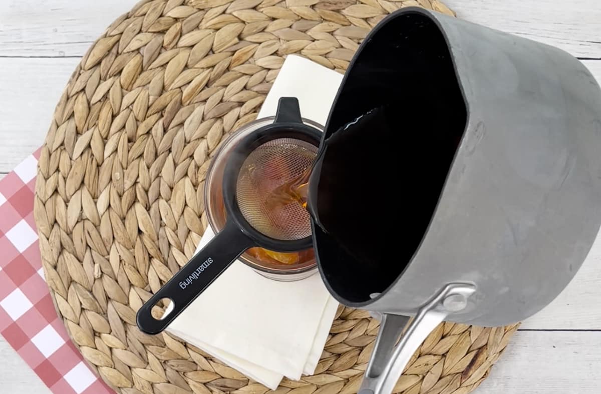 Pouring apple tea into a mug through a strainer.