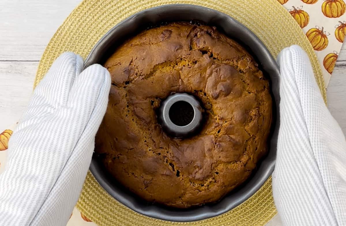Remove a Bundt cake from an oven with oven mitts.