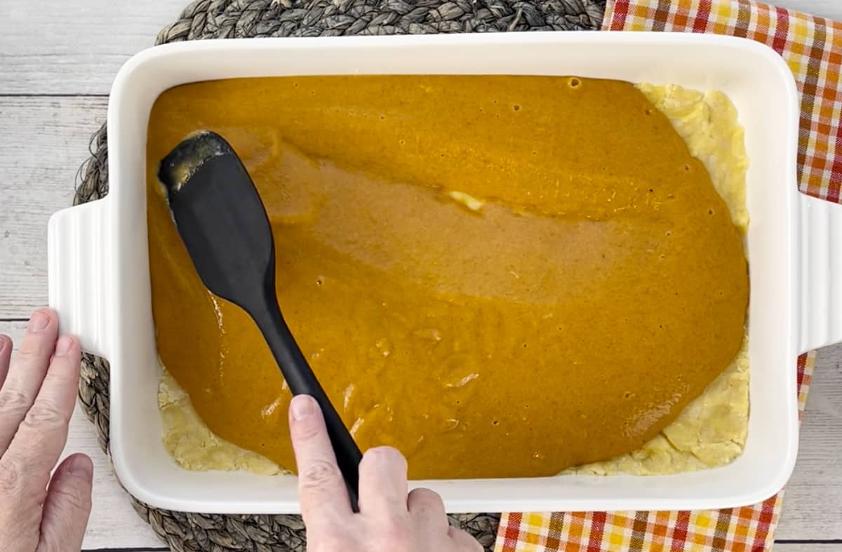 Using a spatula to spread the pumpkin filling on top of the cake.