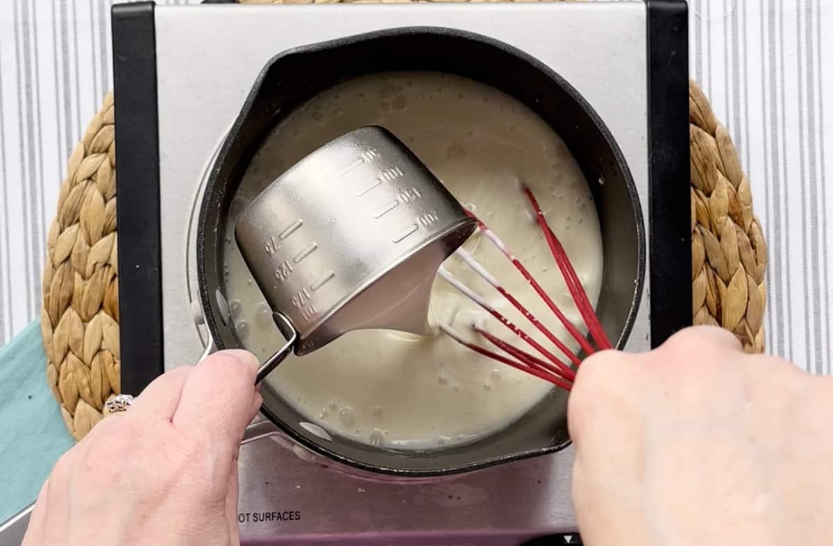 Adding heavy whipping cream to a saucepan on a skillet.
