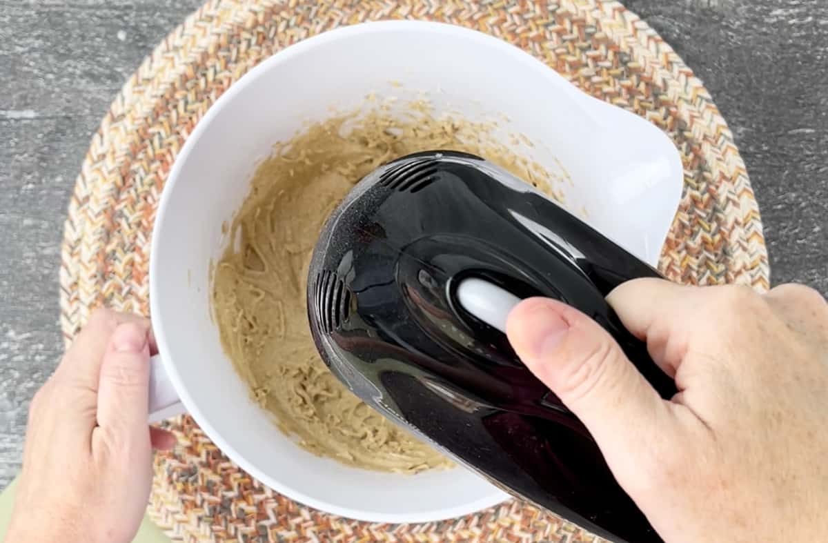 Using a hand mixer to make the cookie dough in a white bowl.