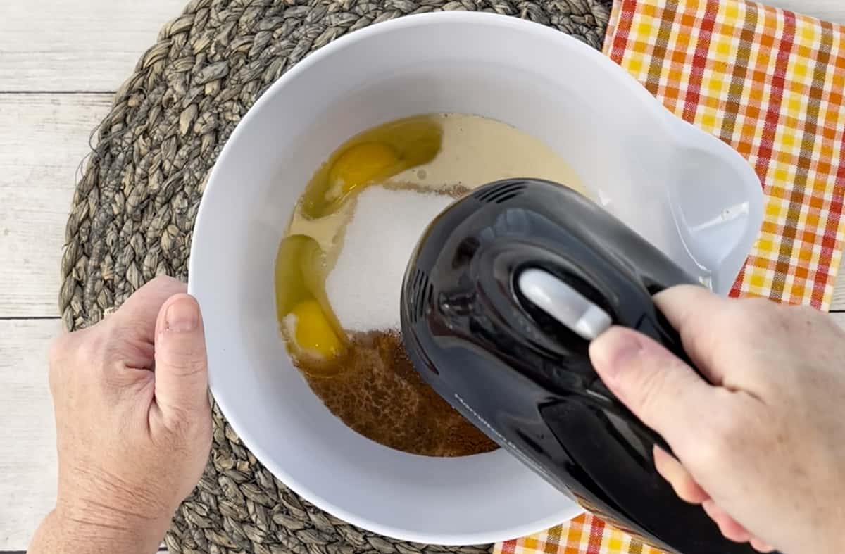 Blending the pumpkin pie filling in a white bowl with a hand mixer.