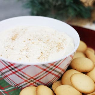 Eggnog cheesecake dip in a plaid Christmas bowl next to vanilla wafers