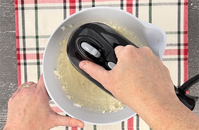 Blending the dip with a black hand mixer on a plaid placemat