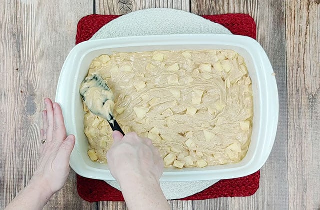 Spreading German apple cake batter into a white baking dish with a spatula