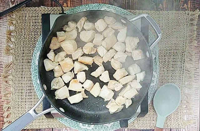 Cubed chicken breast cooking in a deep skillet with olive oil