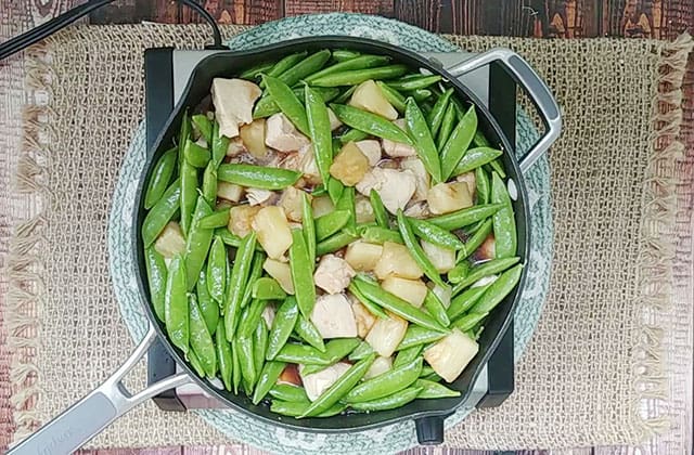 Adding sugar snap peas to a skillet with pineapple chicken