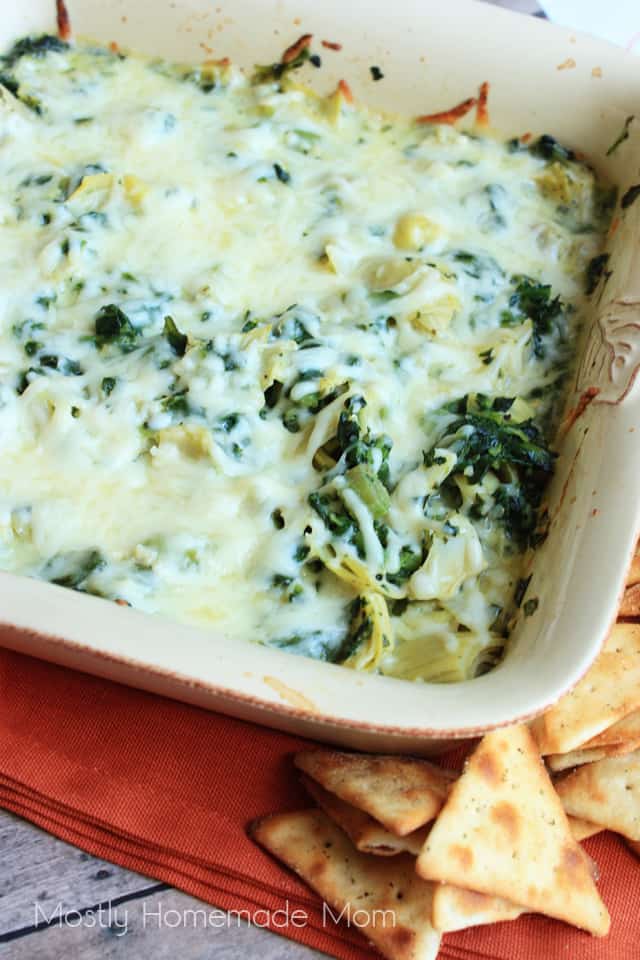 Skinny spinach artichoke dip in a square baking dish on an orange napkin with pita chips