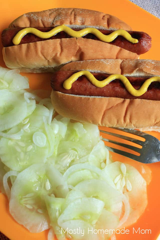 Cucumber salad on an orange plate with a fork next to grilled hot dogs