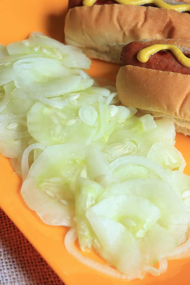 Cucumber salad on an orange plate next to hot dogs