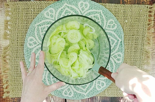 Stirring cucumber salad recipe ingredients in a glass mixing bowl with a wooden spoon