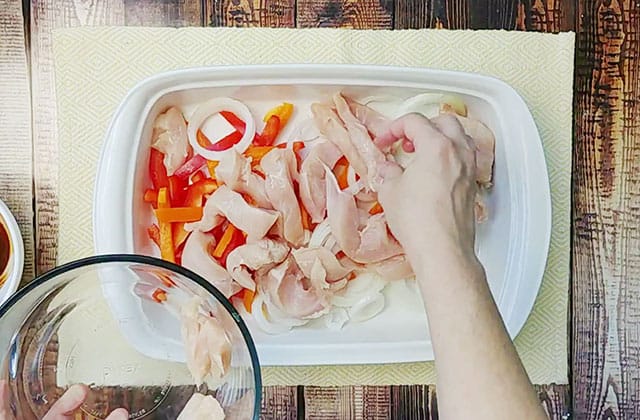 Placing peppers, onions, and chicken slices in a white baking dish