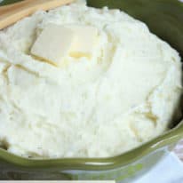 Creamy mashed potatoes in a large green serving bowl with wooden spoon