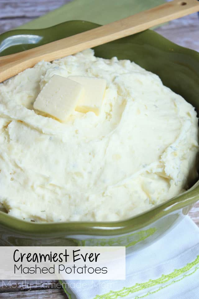 Creamy mashed potatoes in a large green serving bowl with wooden spoon