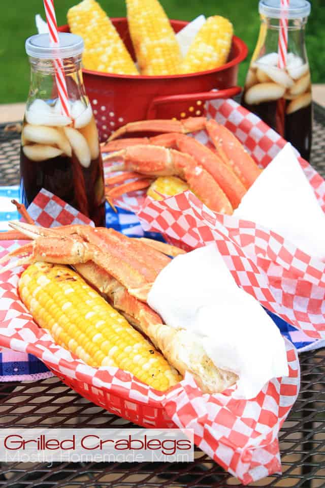 Bundles of grilled crab legs next to corn in red baskets outside